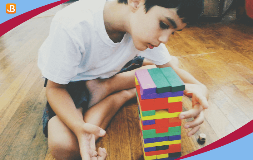 A four-year-old boy is stacking colorful blocks into a tall tower